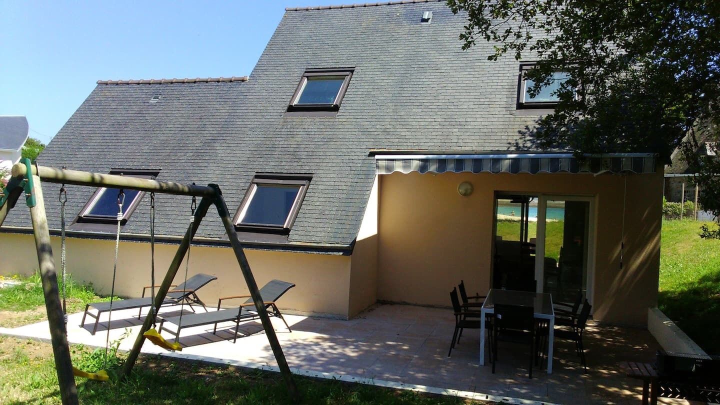 Une maison dotée d’un patio, d’une balançoire et d’un petit espace de repos couvert, avec une table et des chaises.
