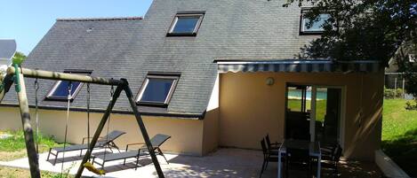 Une maison dotée d’un patio, d’une balançoire et d’un petit espace de repos couvert, avec une table et des chaises.