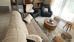 A living room with a sofa, two armchairs, a coffee table, and a kitchen in the background.