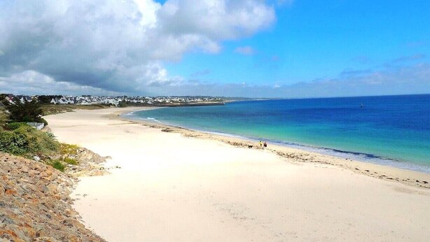 A beach with clear blue water, sandy shore, and a rocky outcrop.