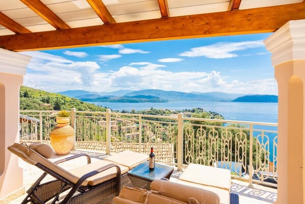 A balcony with wicker furniture, a potted plant, and a view of a lake and mountains. - Villa Frosso - Three Bedroom Villa, Sleeps 6 (Kalami)