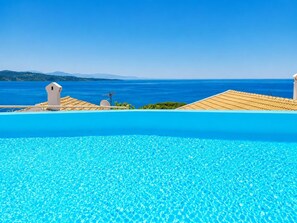 Une piscine d’un bleu éclatant, avec vue sur la mer et les collines lointaines.
