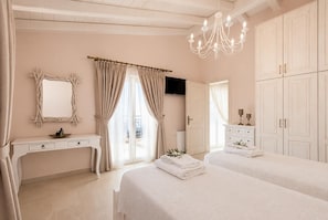Une chambre avec deux lits, une coiffeuse, un lustre et une grande armoire.