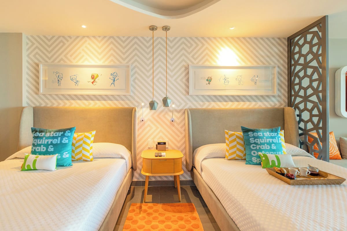 Une chambre d’hôtel avec deux lits, une petite table sur laquelle se trouve un plateau de petit-déjeuner, et des œuvres d’art accrochées aux murs.
