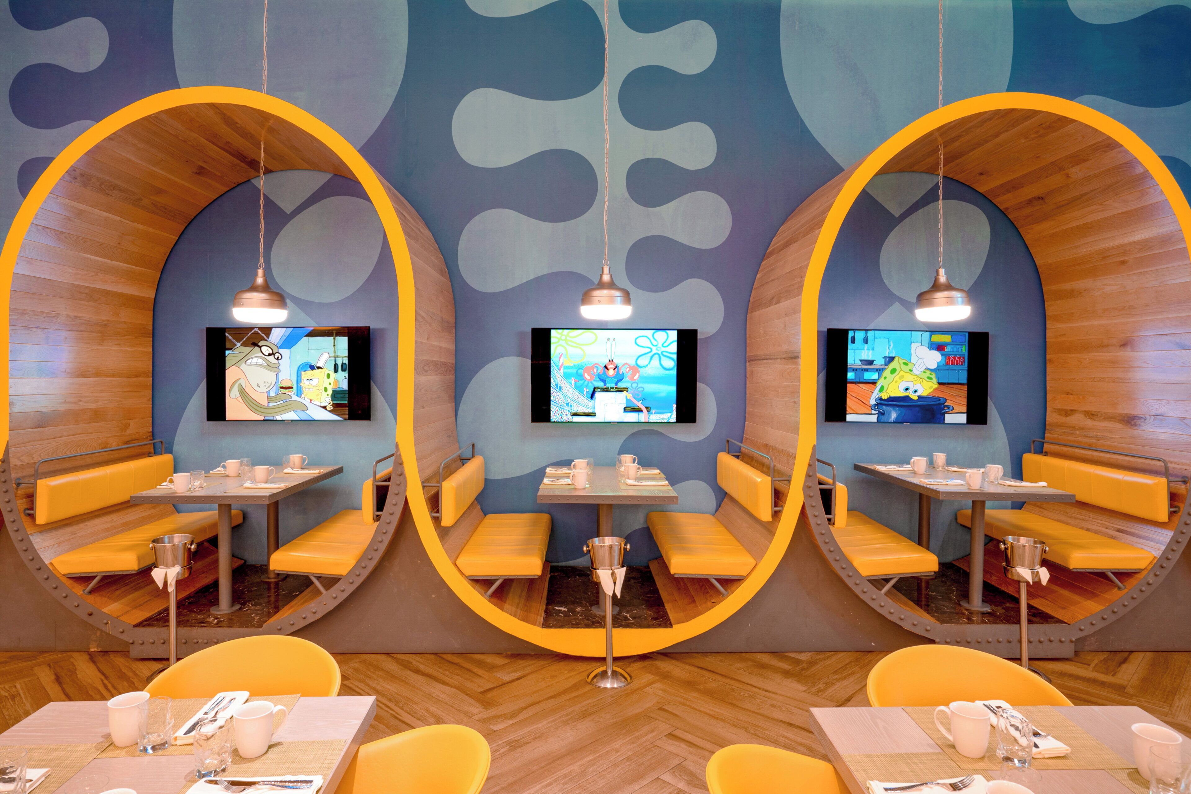 A restaurant with three circular booths, each with a television screen, wooden flooring, and yellow seating.