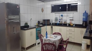 A compact kitchen with white cabinets, a stainless steel refrigerator, a stove, and a dining table with chairs. - House Located in the Center of Guape Mg (Guapé)