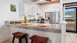 A kitchen with white cabinets, a granite countertop, a ceiling fan, and a view through a glass door. - Lovely Oceanfront 2/Bdrm, 4th Floor Condo with A/C at the Kona Bali Kai Resort (Kailua-Kona)