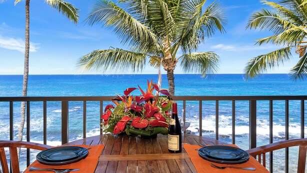 A wooden table with a bottle of wine, a flower arrangement, and a view of the ocean. - Lovely Oceanfront 2/Bdrm, 4th Floor Condo with A/C at the Kona Bali Kai Resort (Kailua-Kona)