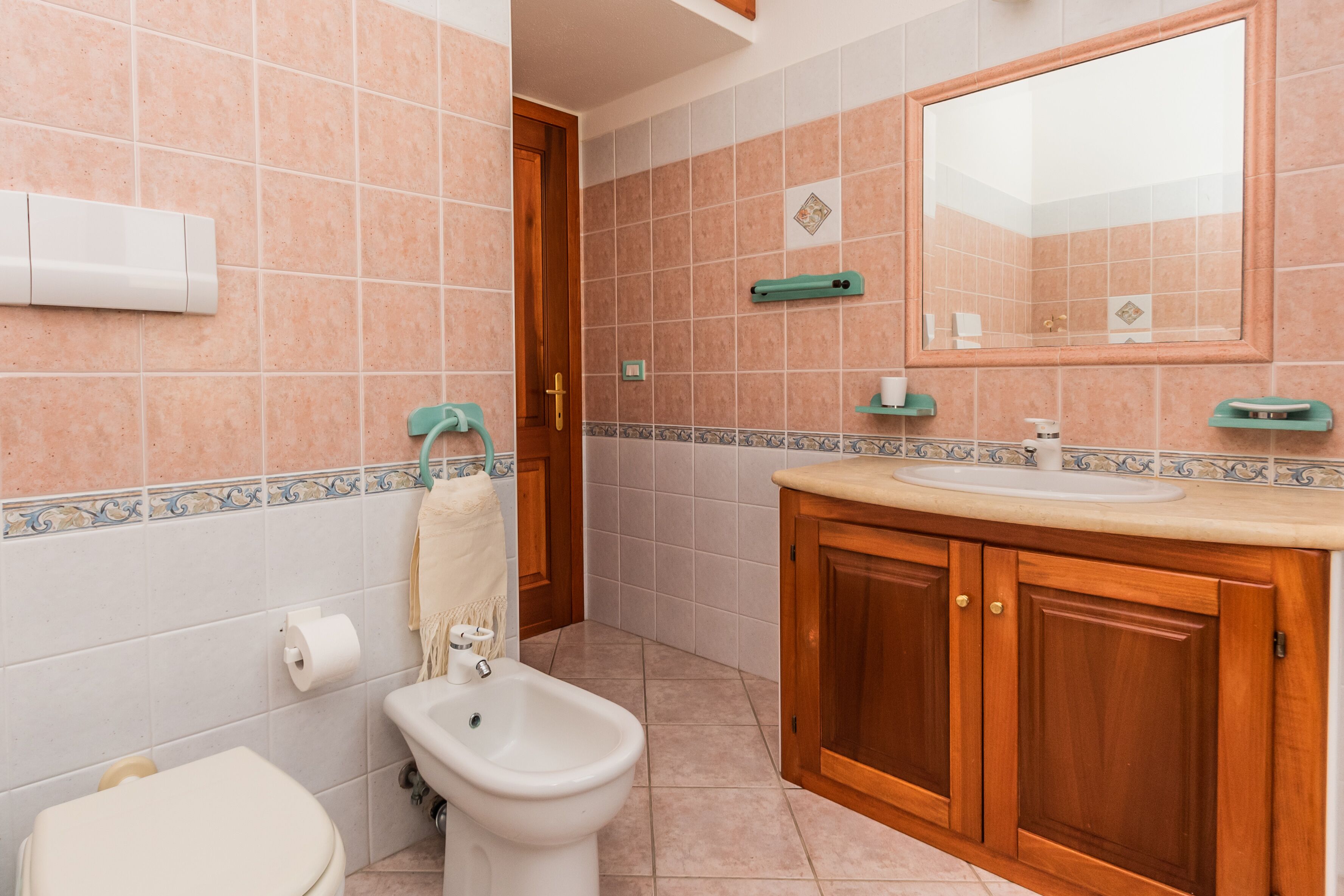 A bathroom with a toilet, bidet, sink, and wooden cabinets.