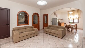 A living room with two beige sofas, a wooden door, and a dining area with a table and chairs. - Casa Marta (orosei)
