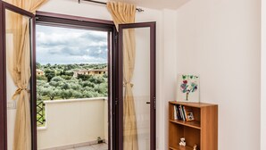 A balcony with a view of a town, a wooden bookshelf, and a door with curtains. - Casa Marta (orosei)
