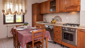 A kitchen with wooden cabinets, a gas stove, a dishwasher, and a tiled backsplash. - Casa Marta (orosei)