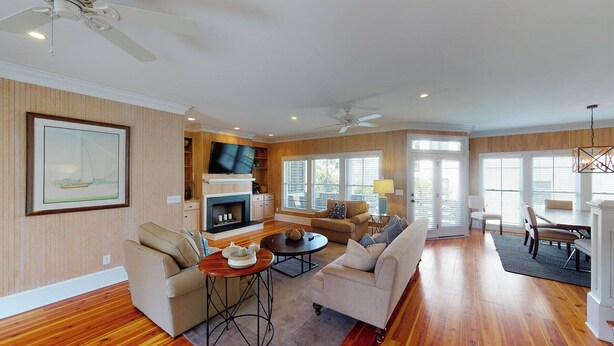 A spacious living room with a fireplace, a television, and a dining area with a chandelier. - Summer Dunes Lane 2-  Updated Wild Dunes 5BR Home  with Partial Ocean View! (Isle of Palms)