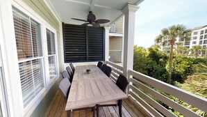 A covered outdoor patio with a wooden table and chairs, a ceiling fan, and a view of a residential area with palm trees. - Summer Dunes Lane 2-  Updated Wild Dunes 5BR Home  with Partial Ocean View! (Isle of Palms)