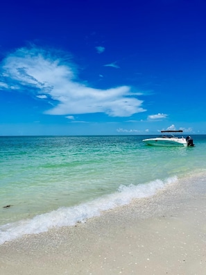 A beach with clear turquoise water, a boat on the shore, and a clear sky. - Resort-Style Pool & Hot Tub! Outdoor TV, Fire Pit & Bikes for Island Adventures! (Marco Island)