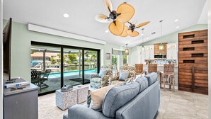 A modern living room with a grey sofa, wicker chairs, and a pool view. - Marco Island Waterfront Escape | Heated Pool + Hot Tub | Private Dock + Fire Pit (Marco Island)