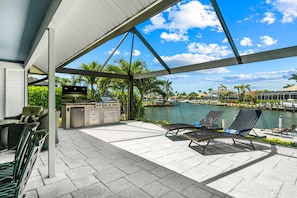 An outdoor patio with a grill, lounge chairs, and a view of a marina. - Resort-Style Pool & Hot Tub! Outdoor TV, Fire Pit & Bikes for Island Adventures! (Marco Island)