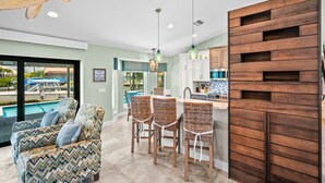 A modern kitchen with wooden cabinets, a dining area with wicker chairs, and a view of a pool. - Marco Island Waterfront Escape | Heated Pool + Hot Tub | Private Dock + Fire Pit (Marco Island)