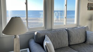 A room with a sofa facing a beach view through two windows. - Recently Renovated OCEANFRONT CONDO Directly on Beach w/2 bedrooms and 2 baths. (Myrtle Beach)