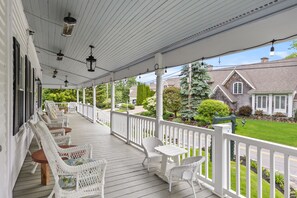 Une véranda couverte, meublée de meubles en osier blancs, donnant sur un quartier résidentiel.
