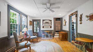 Une pièce chaleureuse avec une grande fenêtre, un ventilateur de plafond, une table en bois et une enseigne indiquant un magasin de vins et fromages.
