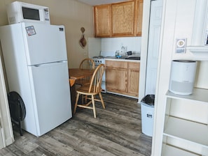 Una cocina funcional con armarios de madera, un refrigerador blanco, un microondas, una estufa y una mesa de comedor con sillas.