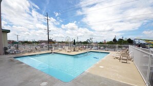 Una piscina rectangular con cerramiento blanco, sillas de descanso y una noria al fondo.