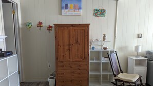 Una habitación con un armario de madera, un sillón mecedora, una estantería con objetos decorativos y un cuadro en la pared.