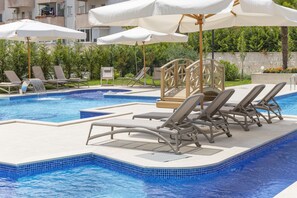 A swimming pool with lounge chairs and umbrellas, surrounded by greenery and a building in the background. - Boutique hotel Momentum by Aycon (Budva)