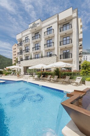 A hotel with a pool, outdoor seating, and a mountain backdrop. - Boutique hotel Momentum by Aycon (Budva)