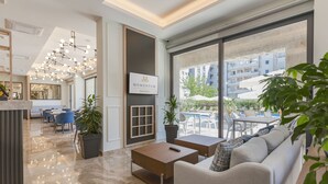 Un hall d’hôtel moderne doté d’un grand espace salon, d’un comptoir d’accueil et d’une vue sur la piscine extérieure.