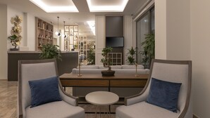 Un salon moderne avec deux fauteuils gris, une table basse ronde et un canapé. Un téléviseur est fixé au mur, et la pièce présente un design contemporain avec une palette de couleurs neutres.
