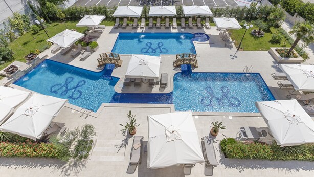 Un espace piscine sur le toit, comprenant plusieurs piscines, des chaises longues et des parasols.