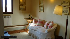 An independent apartment with a white sofa, striped pillows, a table with a bottle and glass, and framed pictures on the wall. - Residence La Pieve Panzano in Chianti with Villa Le Barone pool & tennis access  (Panzano In Chianti)