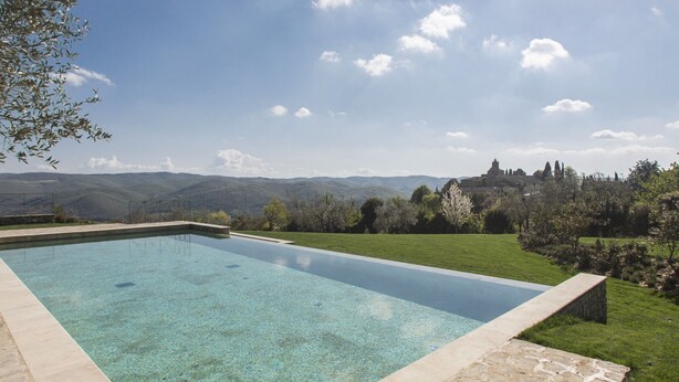 A rectangular swimming pool with clear water, surrounded by a stone border, set against a backdrop of lush greenery and distant mountains. - Residence La Pieve Panzano in Chianti with Villa Le Barone pool & tennis access  (Panzano In Chianti)