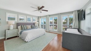A bedroom with a bed, bedside tables, a ceiling fan, large windows, and a view of the outdoors. - Across Beach, Pool, Pool Table,Ping Pong, Golf Cart Rental, Amazing Yard, 7 BR (Destin)