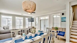 A dining area with a table set for four, a sofa, and a staircase. - Across Beach, Pool, Pool Table,Ping Pong, Golf Cart Rental, Amazing Yard, 7 BR (Destin)