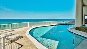 Une piscine à bords incurvés, une rambarde blanche et des chaises longues.