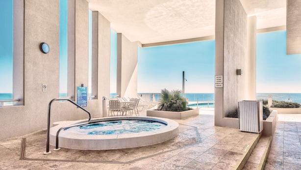 Un espace piscine intérieur moderne, doté d’un jacuzzi, de chaises longues et offrant une vue sur l’océan.