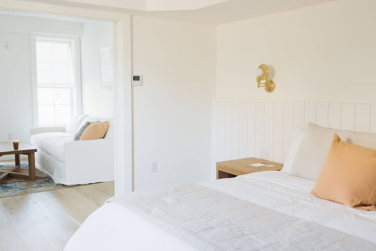 Quarto com cama, mesa de cabeceira, mesa de madeira e sofá branco.