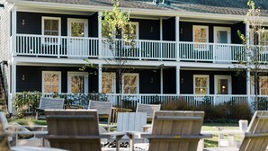 A two-story building with a balcony on the upper floor, outdoor seating with wooden chairs and tables, and a clear view of the surrounding area.