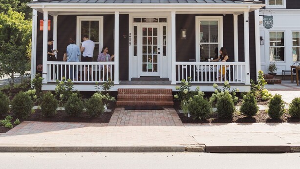 A two-story house with a porch, a front door, and a small garden area.