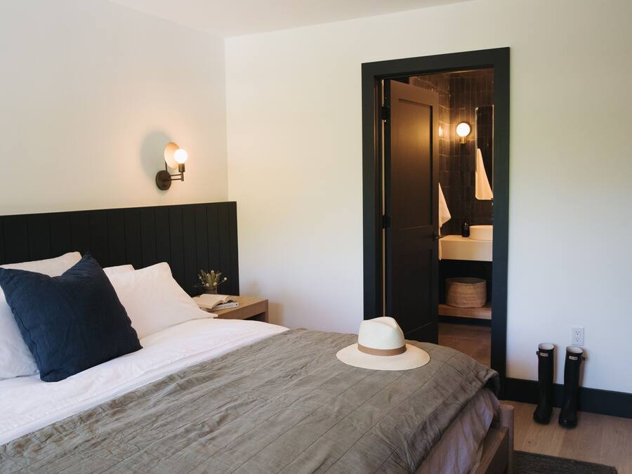 A neatly made bed with pillows, a bedside table with a book and a small plant, and a hat on the bed.