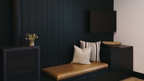A dark wooden panel wall with a mounted flat-screen TV, a bench with cushions, and a small plant in a vase.