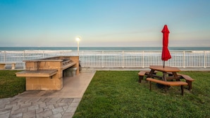 A picnic area with a table and benches, a red umbrella, and a view of the ocean. - Seaside Escape – Ground-Floor Condo with Panoramic Ocean Views, Steps to Beach & Pool 🏝️ (Satellite Beach)