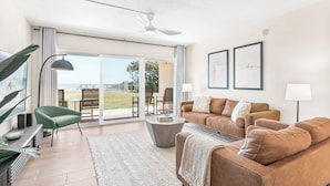 A modern living room with a sofa, a green armchair, a coffee table, and a large window with a view of the outdoors. - Seaside Escape – Ground-Floor Condo with Panoramic Ocean Views, Steps to Beach & Pool 🏝️ (Satellite Beach)