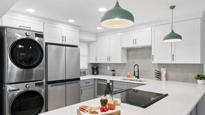 A modern kitchen with stainless steel appliances, a central island with food items, and pendant lighting. - Seaside Escape – Ground-Floor Condo with Panoramic Ocean Views, Steps to Beach & Pool 🏝️ (Satellite Beach)