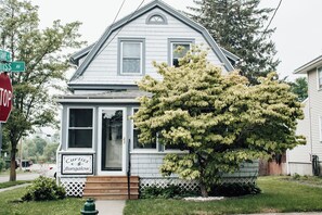 Une maison à deux étages avec un porche à l’avant, une enseigne indiquant « Curtiss Bungalow », et un grand arbre devant.