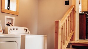 Ein Waschbereich mit Waschmaschine und Trockner, Holzstufen und einem Spiegel an der Wand.