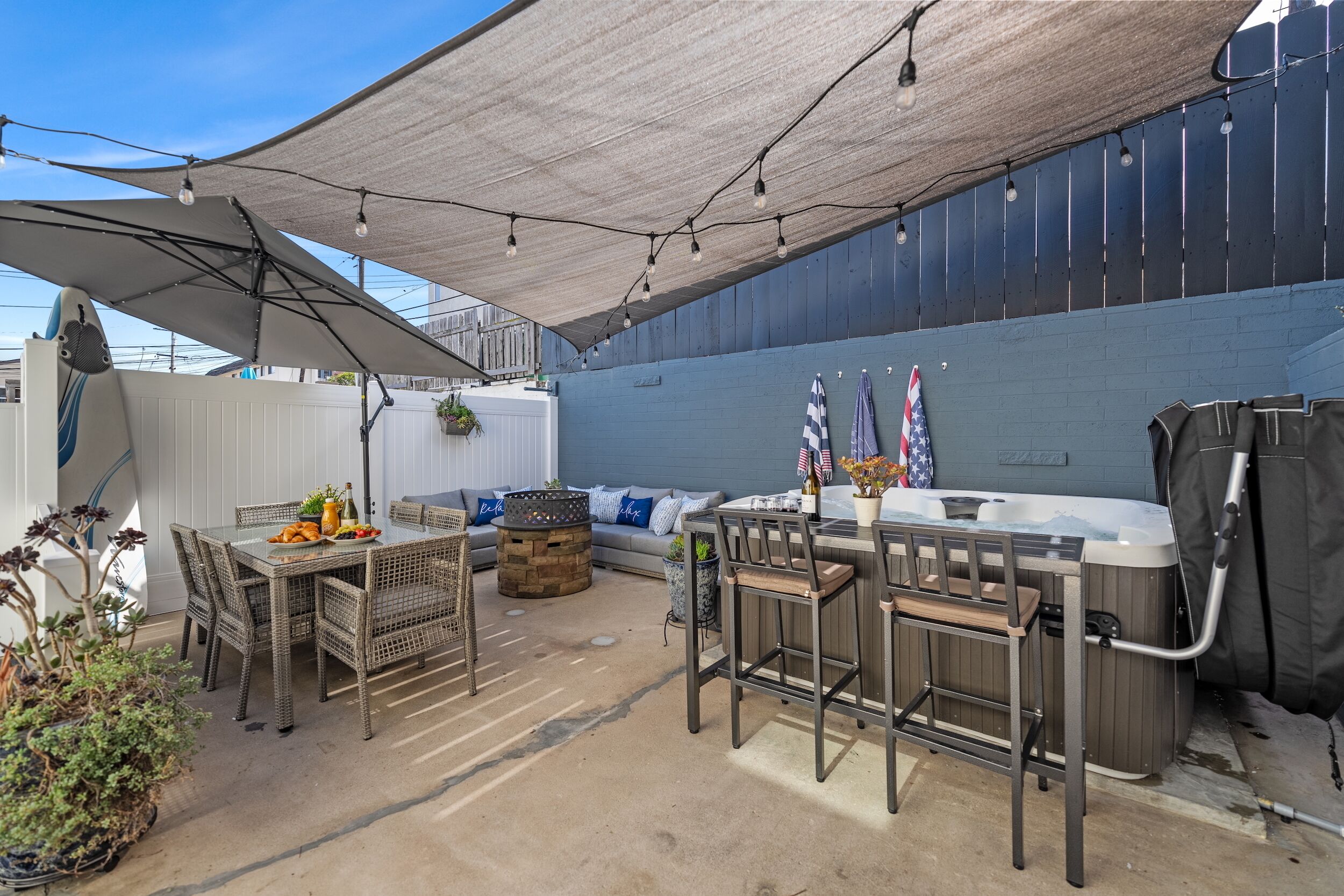 An outdoor patio area with a dining table, chairs, a hot tub, and a covered seating area.